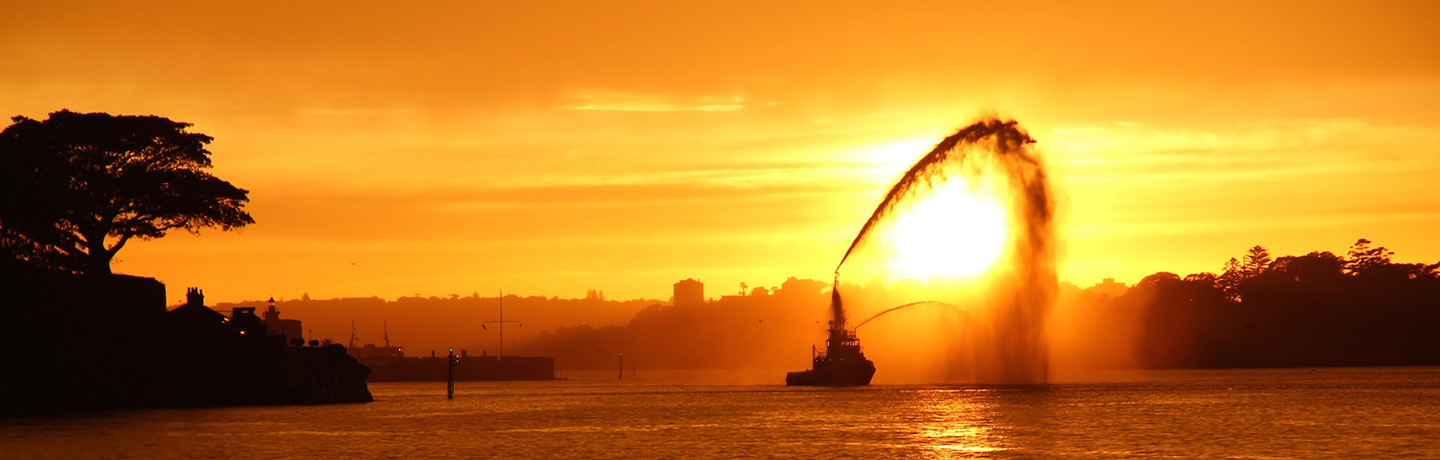 Tug vessel demonstrating water display at sunset